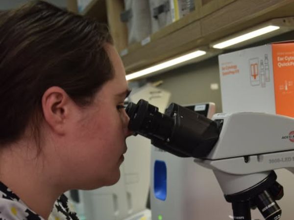 A woman peers intently through a microscope